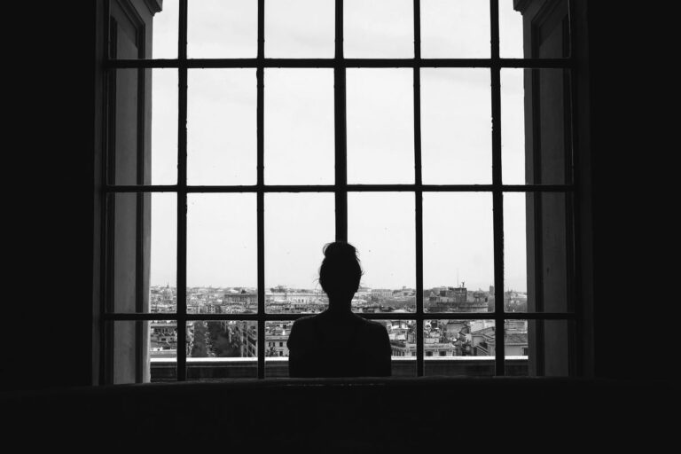 black-white-shot-lonely-female-standing-front-windows-looking-buildings_result