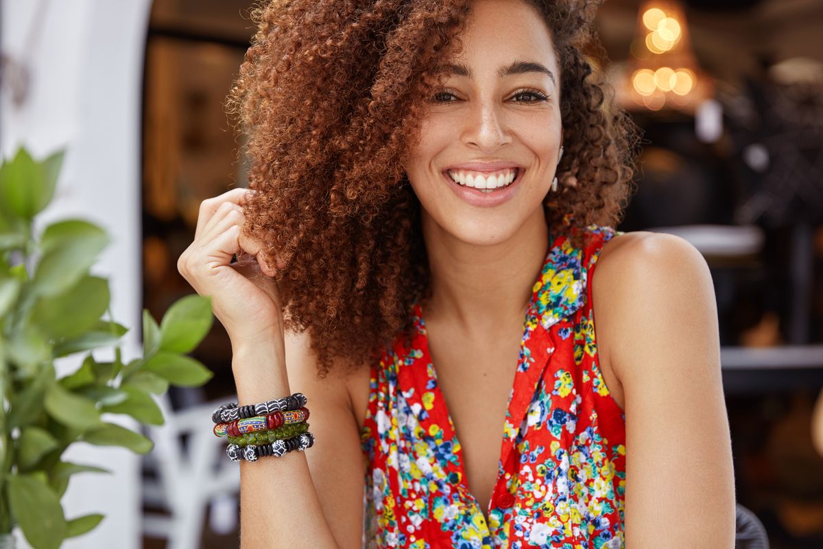 portrait-good-looking-happy-dark-skinned-female-with-curly-hair-shining-broad-smile-demonstrates-positive-emotions-wears-stylish-bright-blouse_result