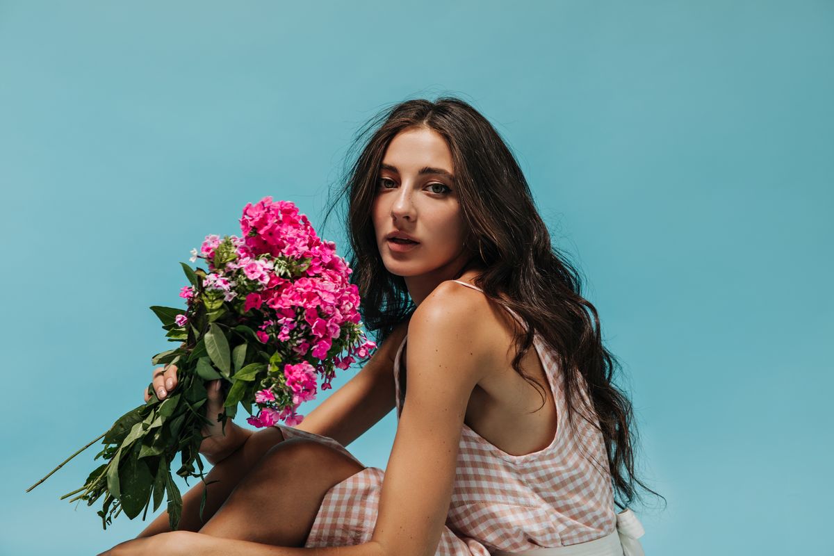 wonderful-girl-with-wavy-hair-modern-plaid-light-clothes-holding-pink-flowers-looking-into-camera-isolated-background_result